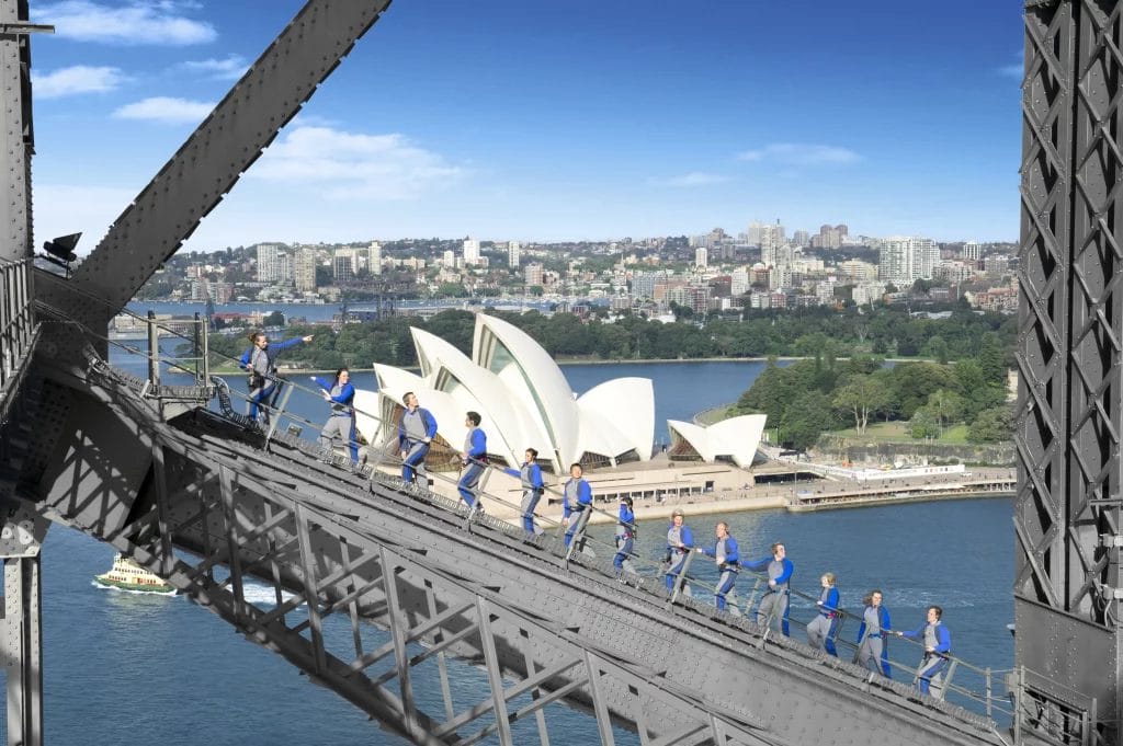 A group of people climbing the Sydney Harbour Bridge with the Opera House in the background.