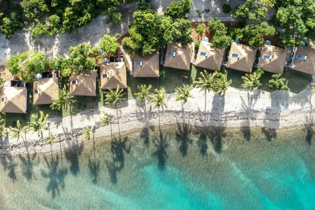 Aerial of Elysian Retreat individual huts, overlooking a pebbled beach fringed with palm trees