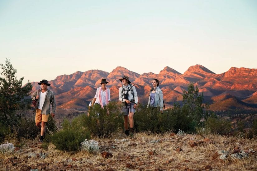 Small group of guests walking through the Flinders Ranges bushland with the mountains lit up in late afternoon light