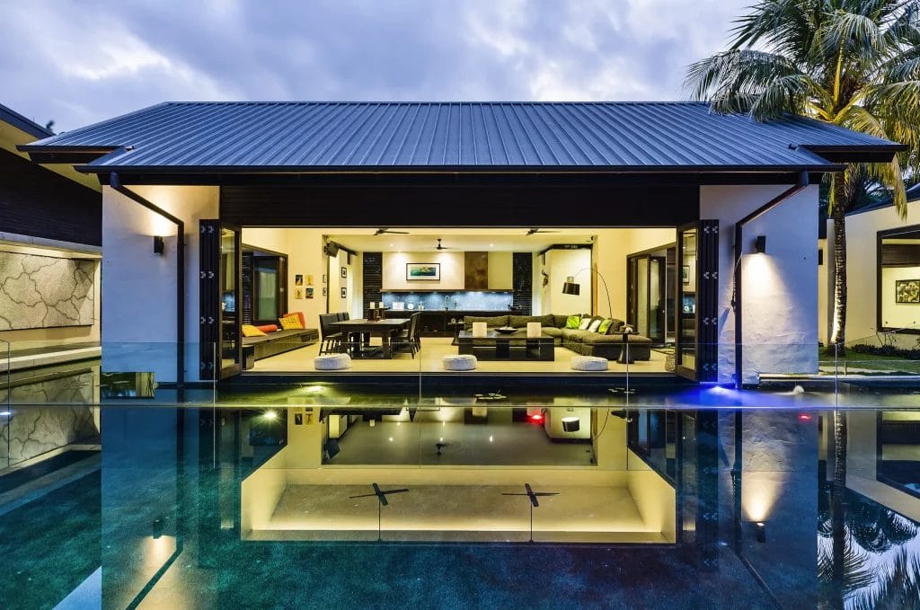 Exterior of Dune Port Douglas private home’s pool and open plan living/kitchen area illuminated in early evening light
