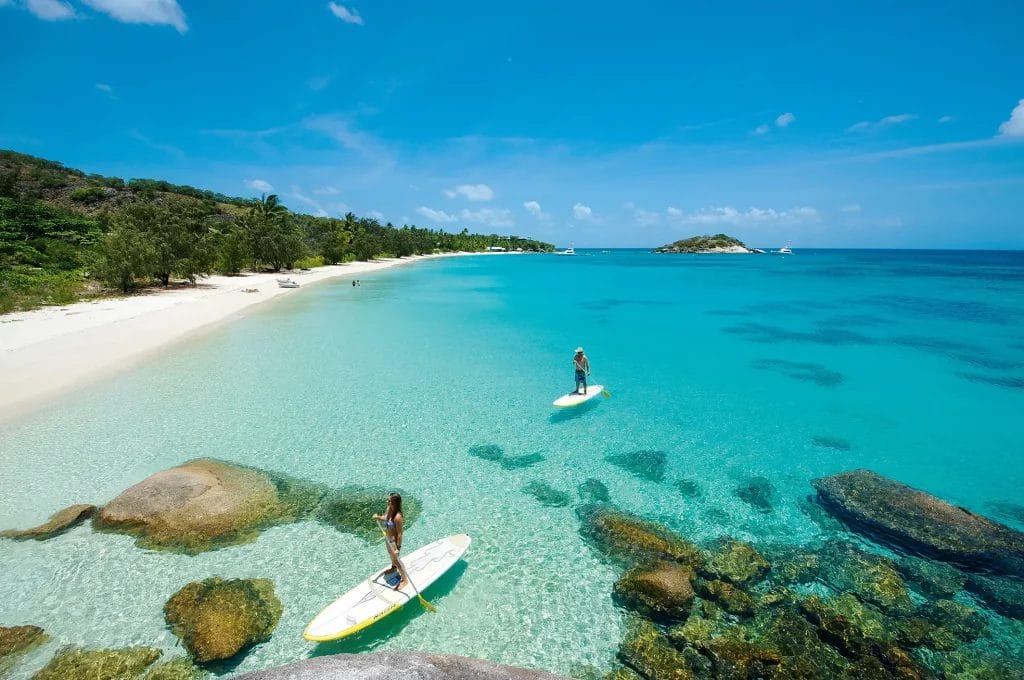 Two people on stand-up-paddleboards stand on crystal clear water