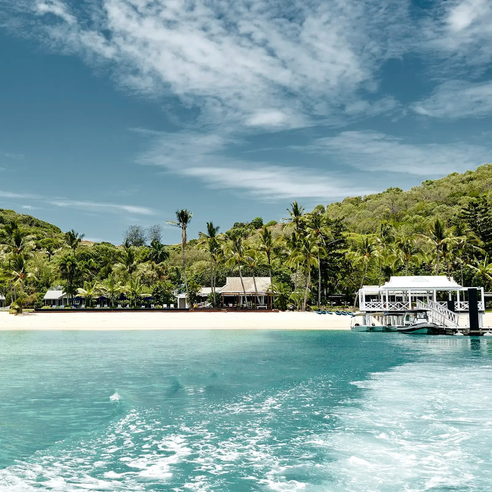 Views of Orpheus Island Lodge from the water, flanked by tropical green palms and white sand