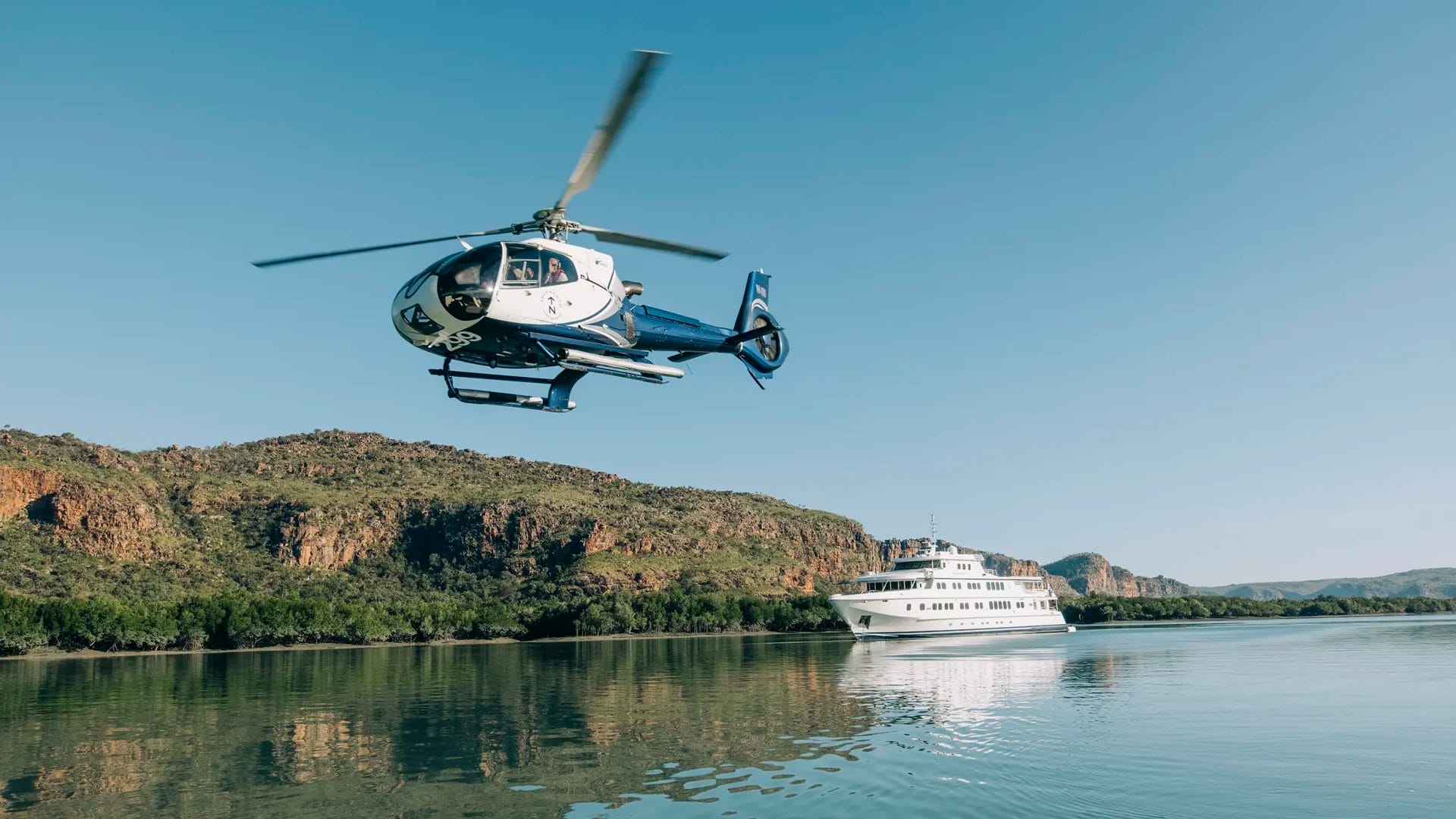 Helicopter in flight over waters in the Kimberley with True North vessel in the background